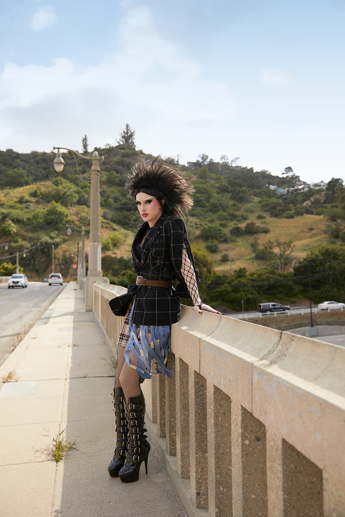 Jesse Clark in punk inspired drag leaning against a hand rail on a bridge over a freeway